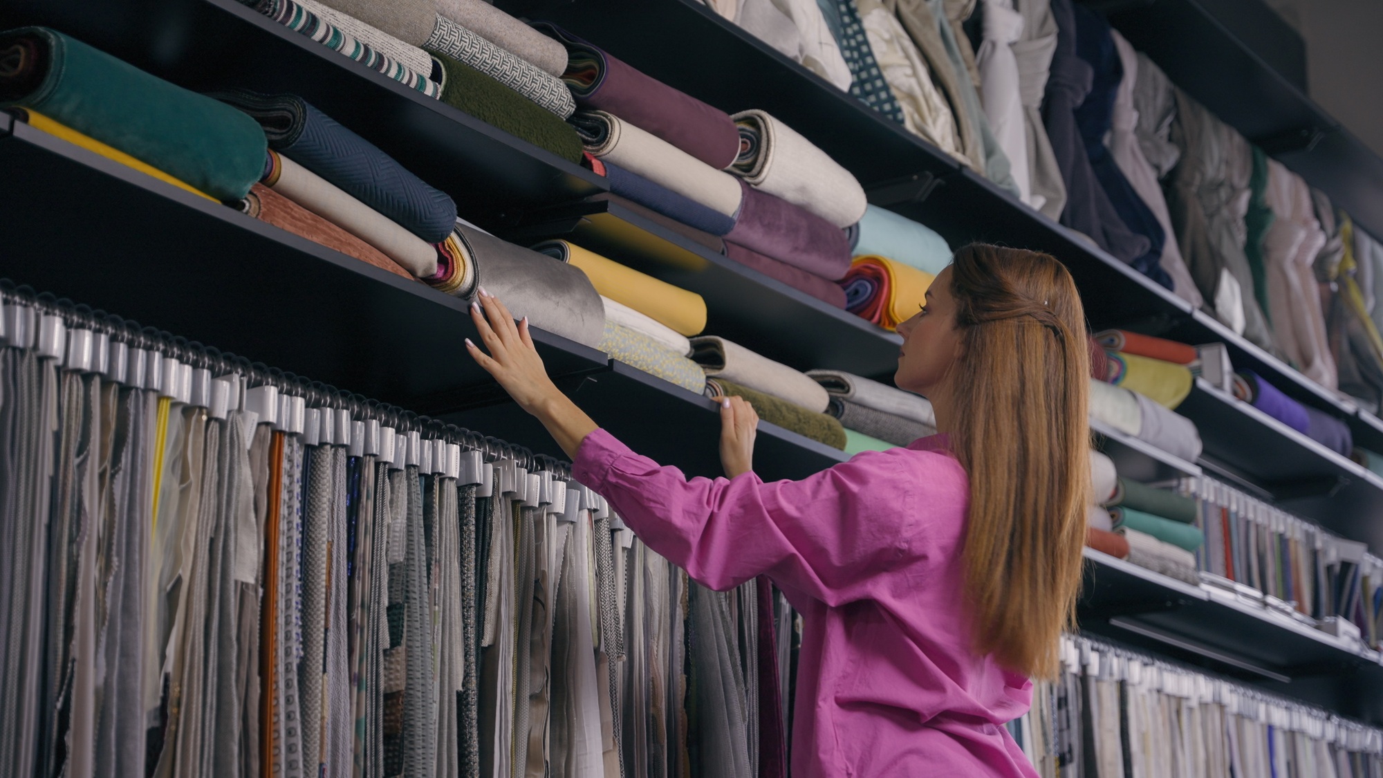Caucasian woman shopper customer choosing fabrics on shelves in cloth store girl shopping choose